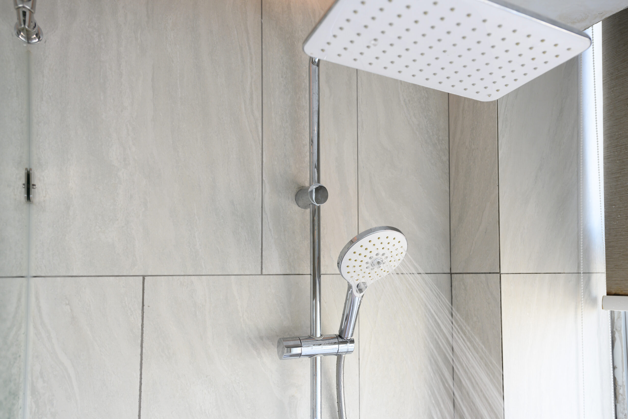 Image of a shower head in a modern bathroom with water drops flowing